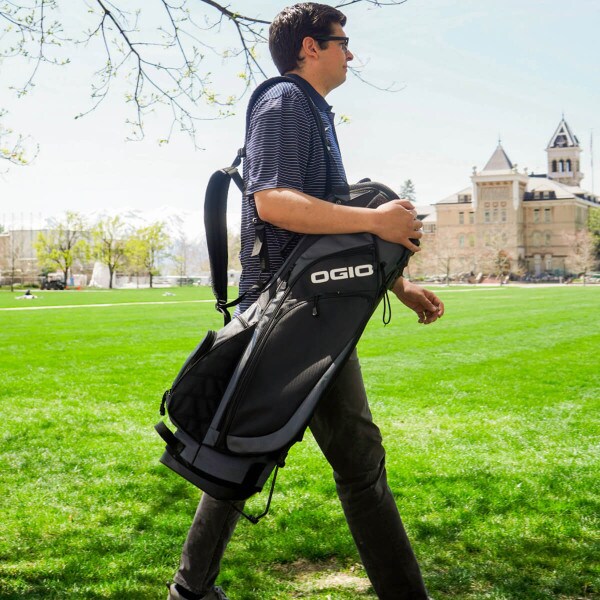 A young man carrying a golf bag across The Quad.